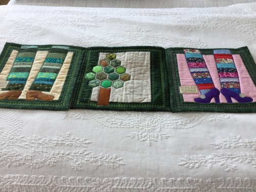 3 small quilts with a dark green border. 2 depicting a pair of legs and shoes and one depicting a tree