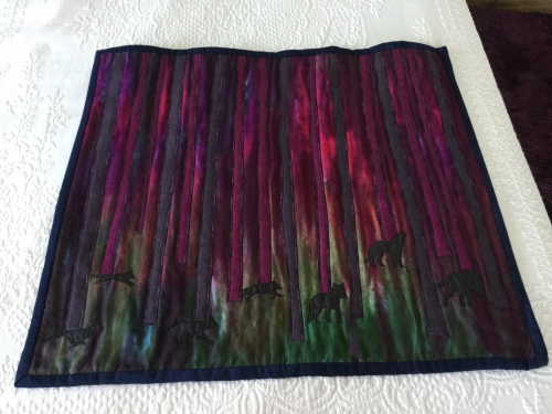 Square quilt depicting a forest of trees in silhouette with a dark pink sky and a number of animals
