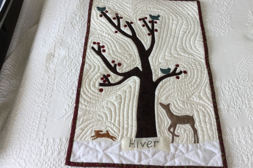 Small quilt laid on a larger white quilt, depicting a tree with animals either side